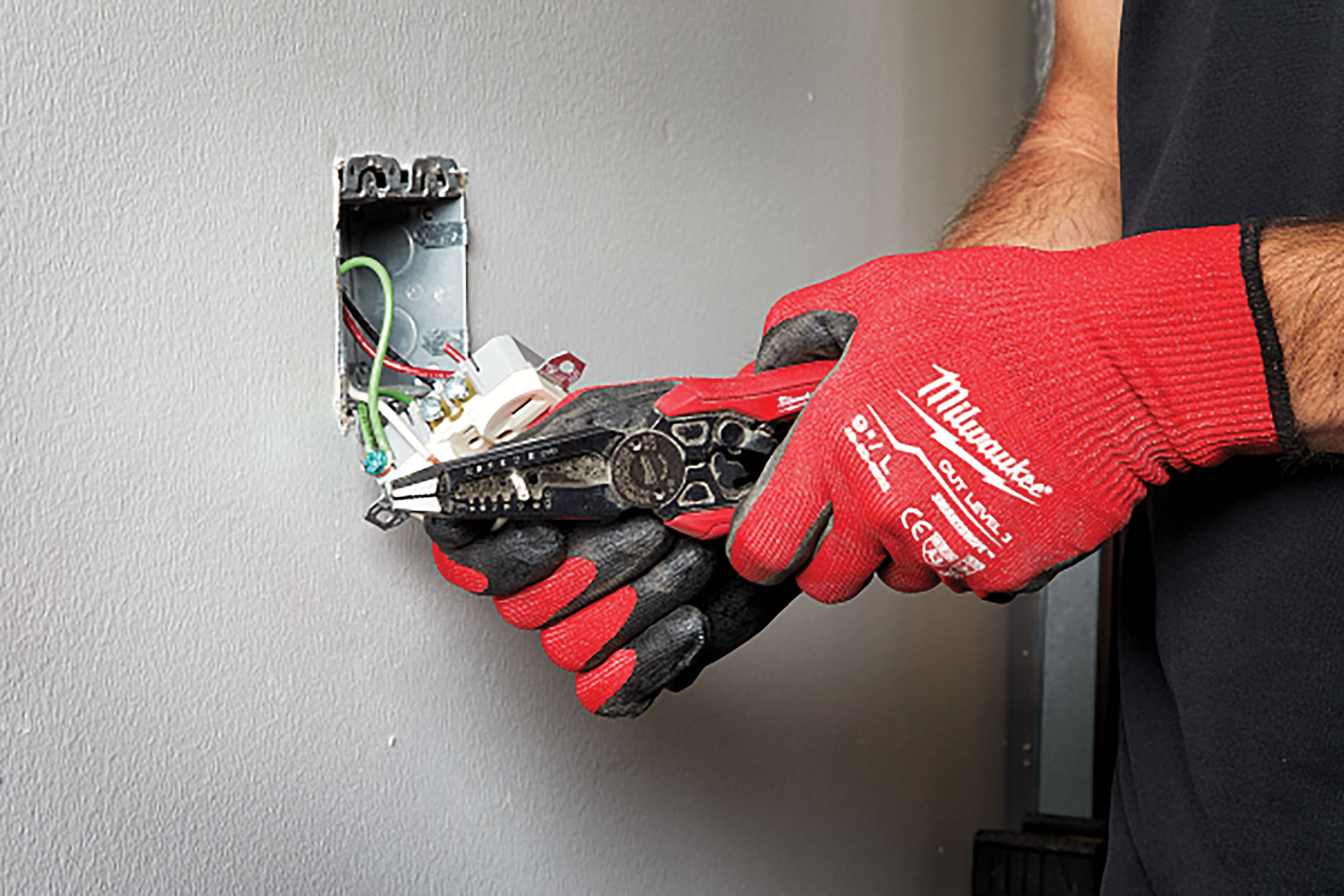 Red gloved hands use combination pliers on a wall outlet. Image by Milwaukee Tool.