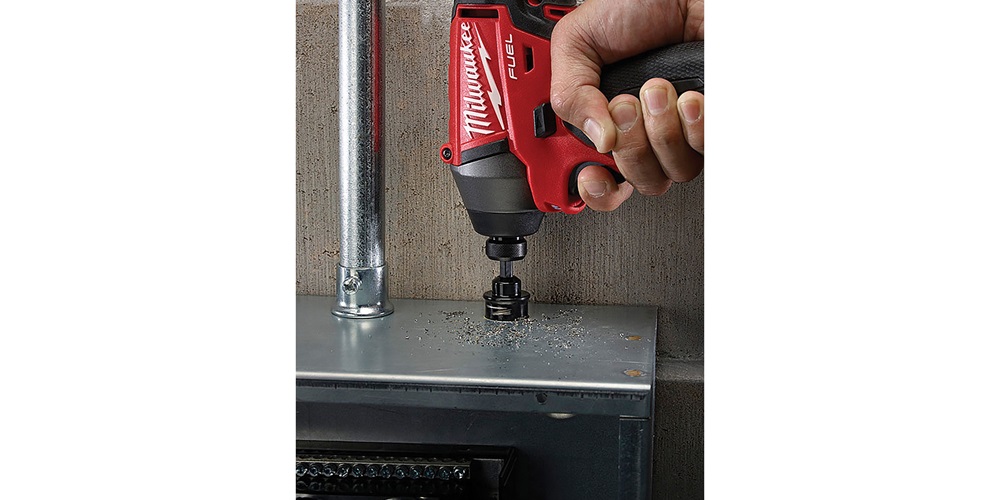 A hand presses a red Milwaukee hole saw against metal. Image by www.milwaukeetool.com.