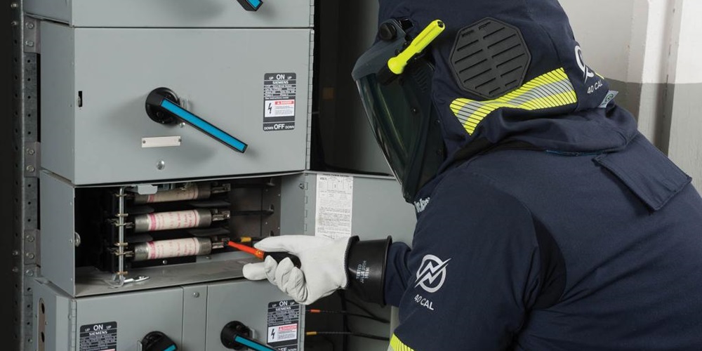 A worker in full PPE works on an electrical box. Image by Enespro.