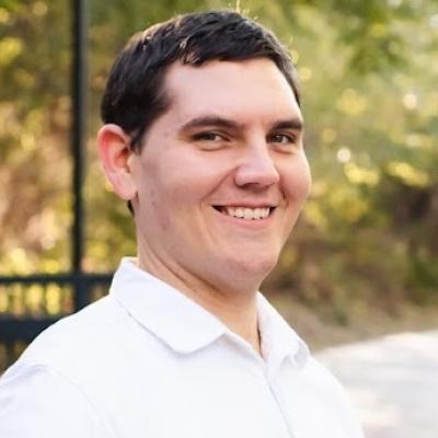 A white man with short brown hair and a white collared shirt smiles at the camera
