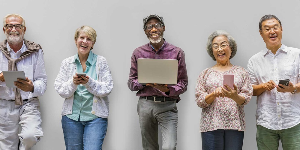 Five smiling seniors hold electronic devices in front of a gray background. Image by Shutterstock.