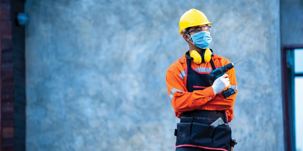 A worker wears a blue surgical mask in front of a blue background. Image by stock.adobe.com / Visoot.