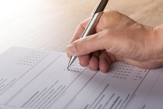 A hand holding a silver pen fills out a survey.  Image by Andreas Breitling from Pixabay