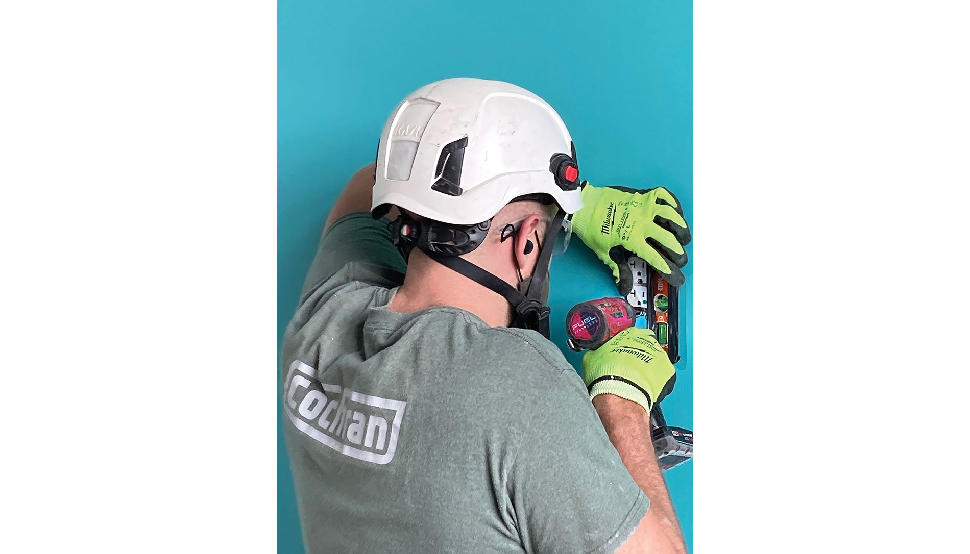 A man in a Cochran shirt and protective gear works on a wall outlet. Image by Cochran Inc.