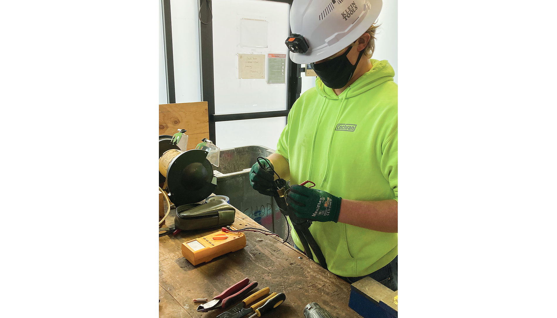 A worker in a Cochran hoodie and protective gear works with cables on a workbench. Image by Cochran Inc.