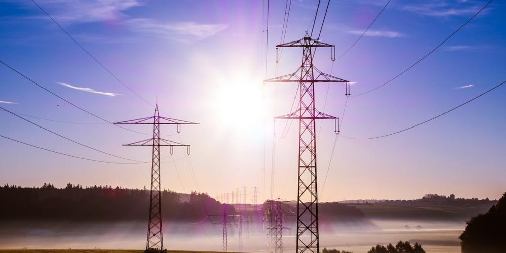 Power towers silhuetted against sun and foggy fields. Image by Shutterstock.
