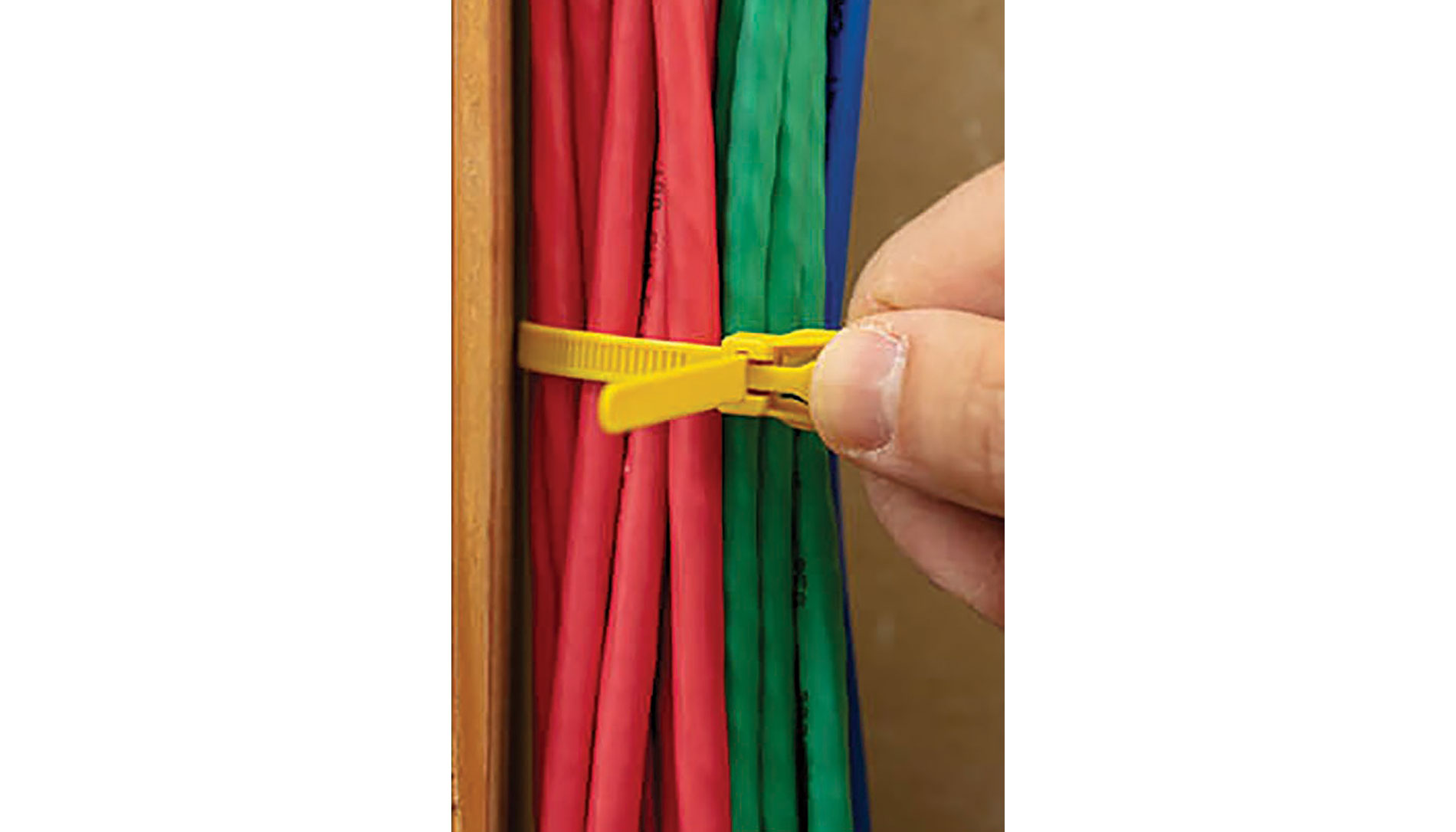 A hand holds a yellow reusable cable tie around multicolored cables. Image by Retyz.