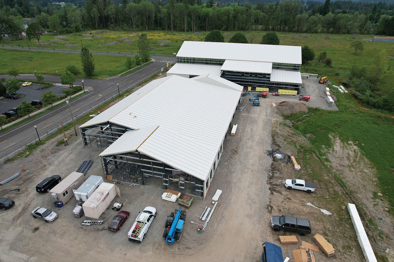 Aerial photo of two white barn-like buildings in a meadow surrounded by cars and trees. Image by Northwest Line JATC.