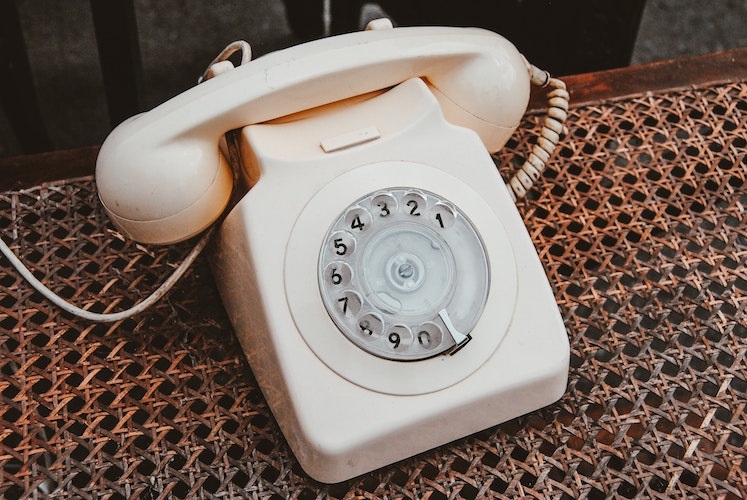 A white rotary phone on a rattan surface / Hello I'm Nik on Unsplash
