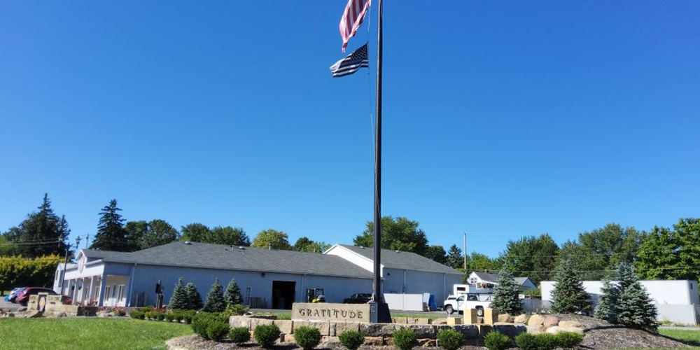 Flagpole surrounded by grass, a low building and a sign reading Gratitude. Image by Santon Electric.