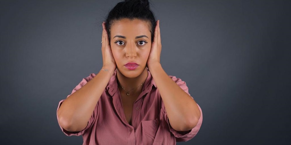 A woman in a pink shirt covers her ears. Image by Shutterstock / Jihan Nafiaa Zahri.