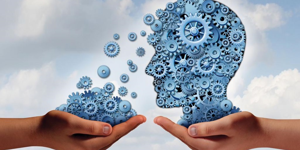 Against a cloudy sky, one hand holds an illustration of a head made of cogs, and another hand holds cogs. Image by Shutterstock / Lightspring.