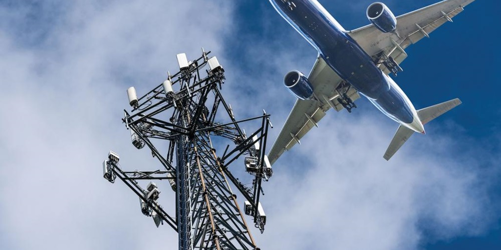 A plane flies past a cell tower. Image by Shutterstock / Steve Heap.