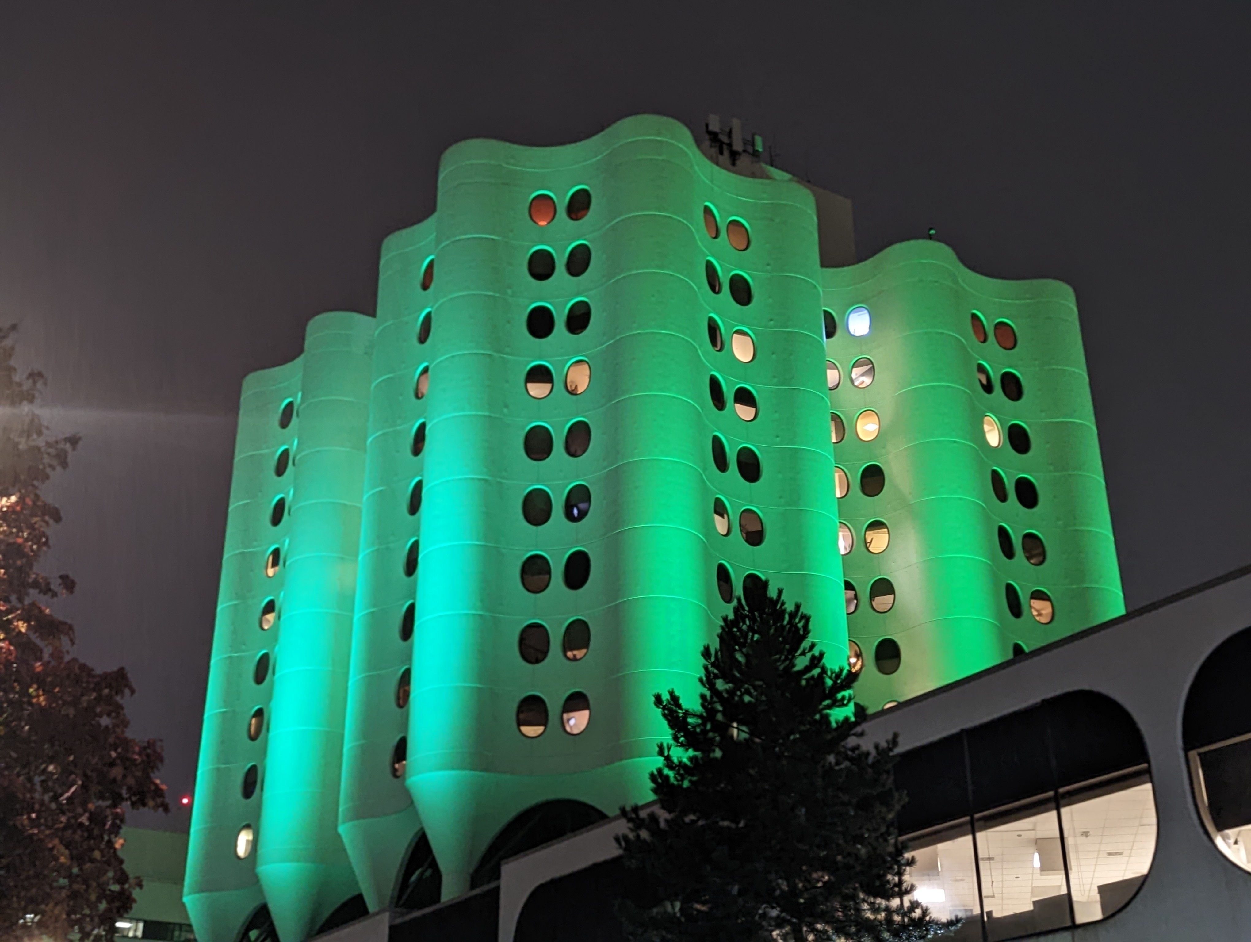 Curving tower blocks with green lighting against a night sky. 