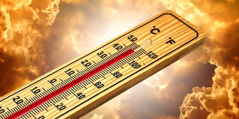 Wooden thermometer measuring over 100 degrees Fahrenheit against yellow clouds.