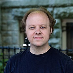 A man, Timothy Johnson, smiles in front of a stone building. Image by Timothy Johnson.