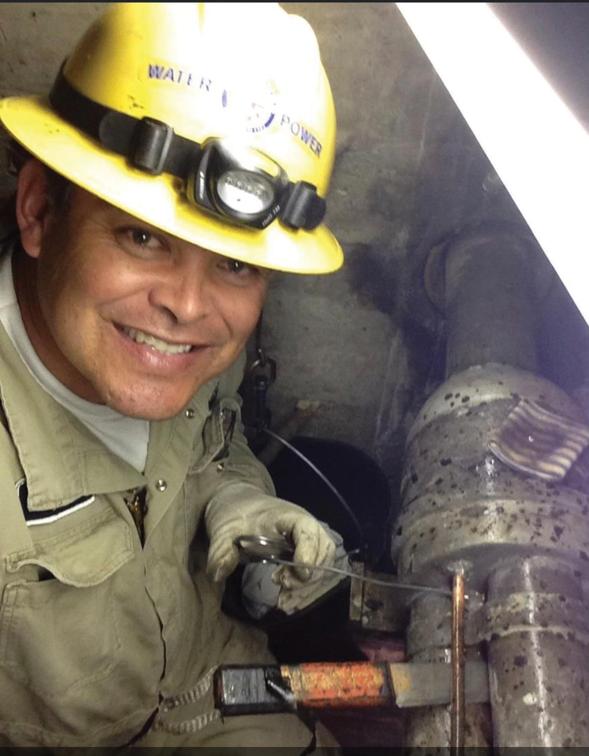 A man in a hard hat, Tony Pinon, smiles next to a series of pipes. Image by Tony Pinon.
