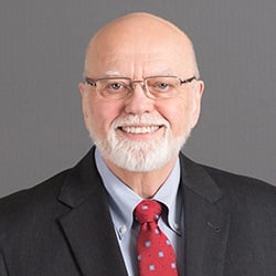 A man, Wayne Moore, smiles in front of a gray background. Image by Wayne Moore.