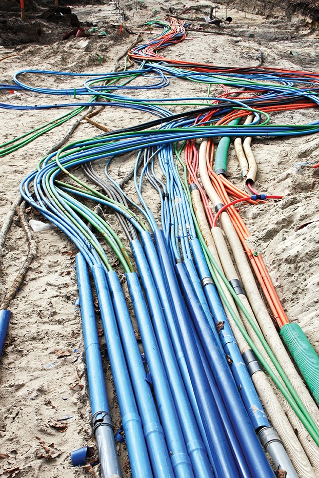Underground electrical conduits and cables in blue, green and orange protective conduit arranged for installation at a construction site.