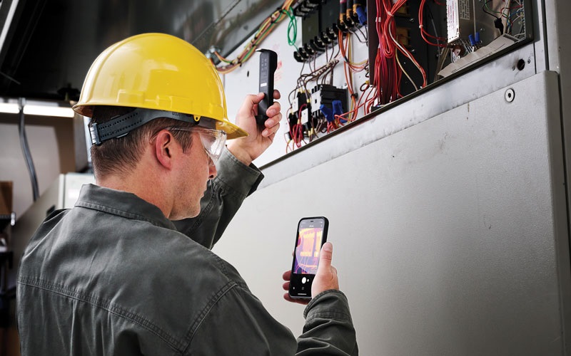 Electrician holding a thermal imager to an electric box and viewing it on a smart phone