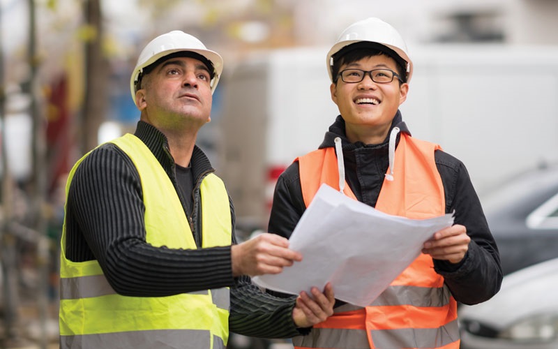 Two construction workers looking up while holding a blueprint