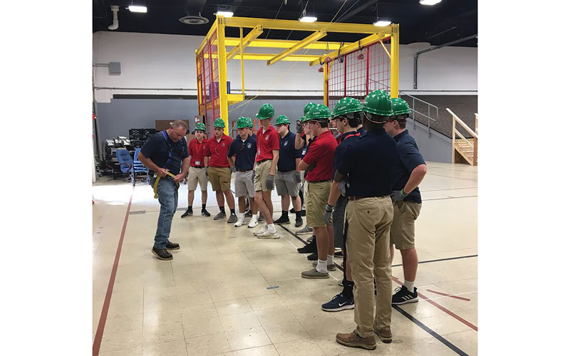 Students watching a constructor put on a safety harness