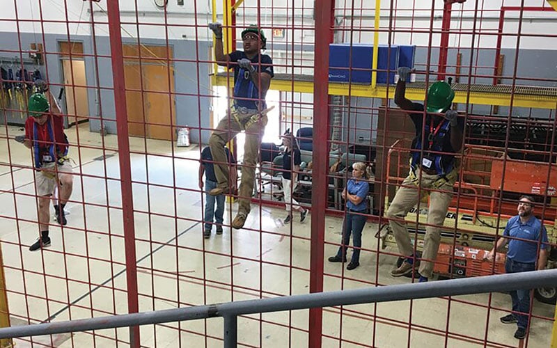 Students wearing safety harnesses and climbing on a practice structure