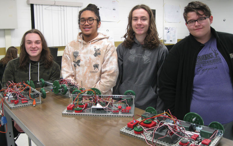 Four high school students in a classroom presenting their engineering projects